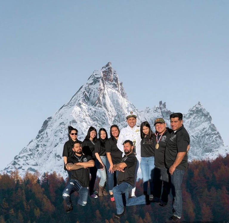 A group of smiling friends posing for a portrait in front of a snowy mountain peak.