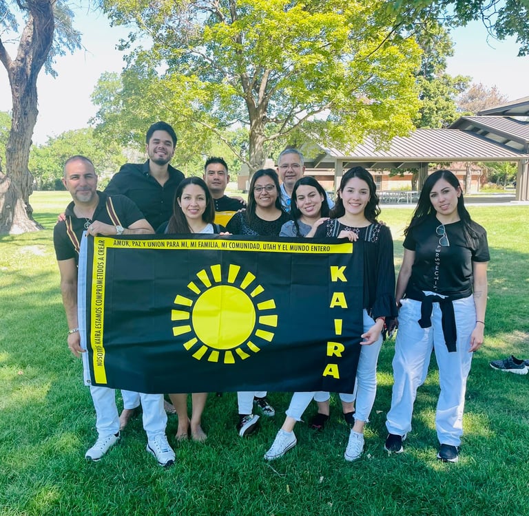 A diverse group of people holding a black Kaira sun flag at a sunny outdoor community park.