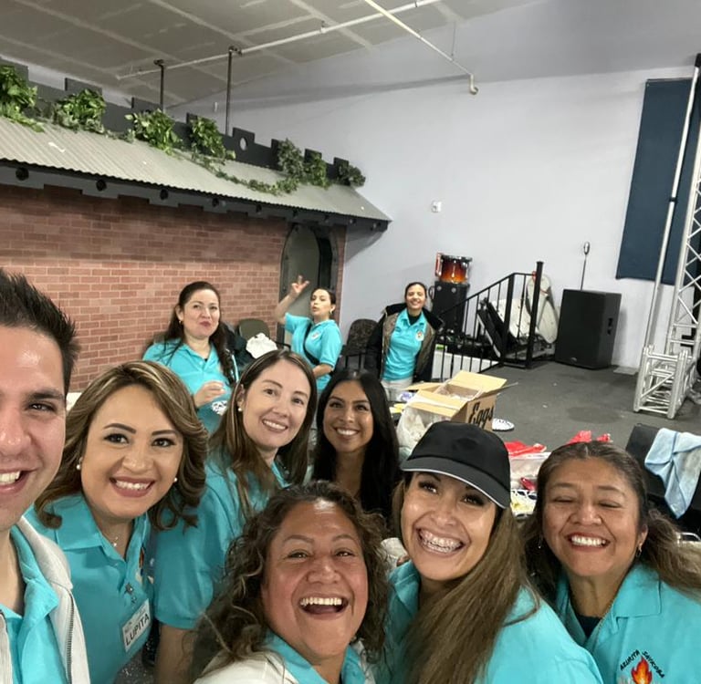 A cheerful group of event volunteers in matching blue shirts posing for a group selfie indoors.