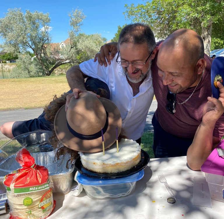 Friends gathered outdoors for a birthday celebration with a frosted cheesecake and candles.