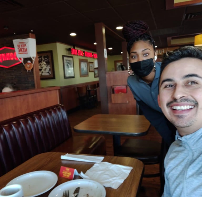 A happy customer takes a selfie with a waitress wearing a mask inside a Denny's restaurant.