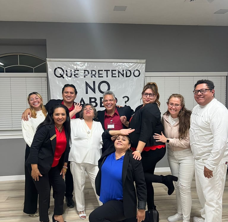 Diverse professional group posing by a Que Pretendo No Saber banner for team building.
