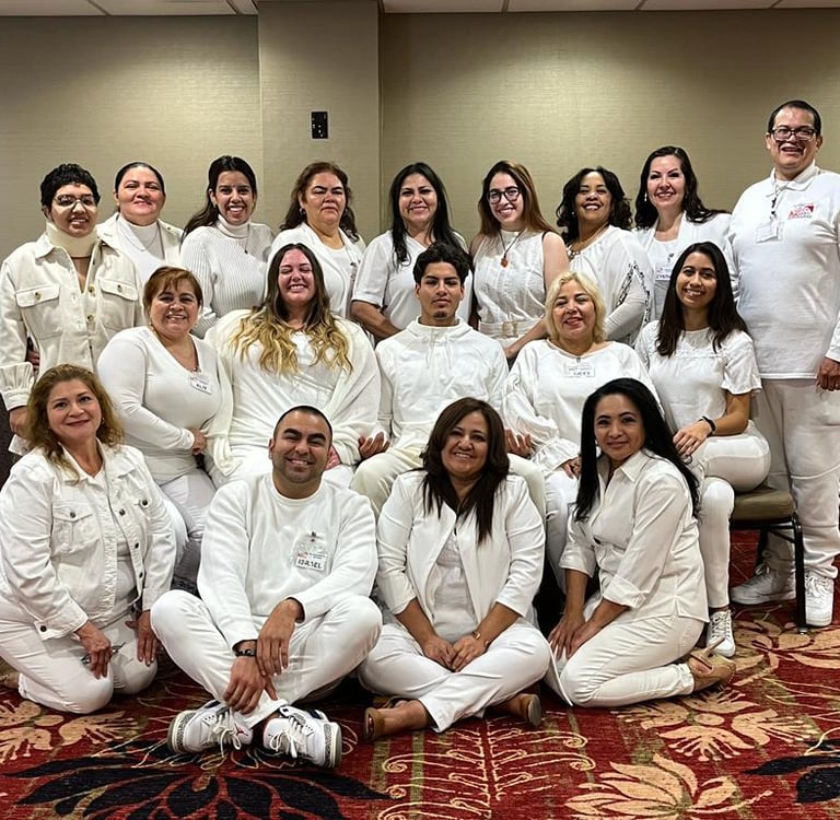 Diverse group of smiling people in white professional attire posing for a team photo in a conference room.