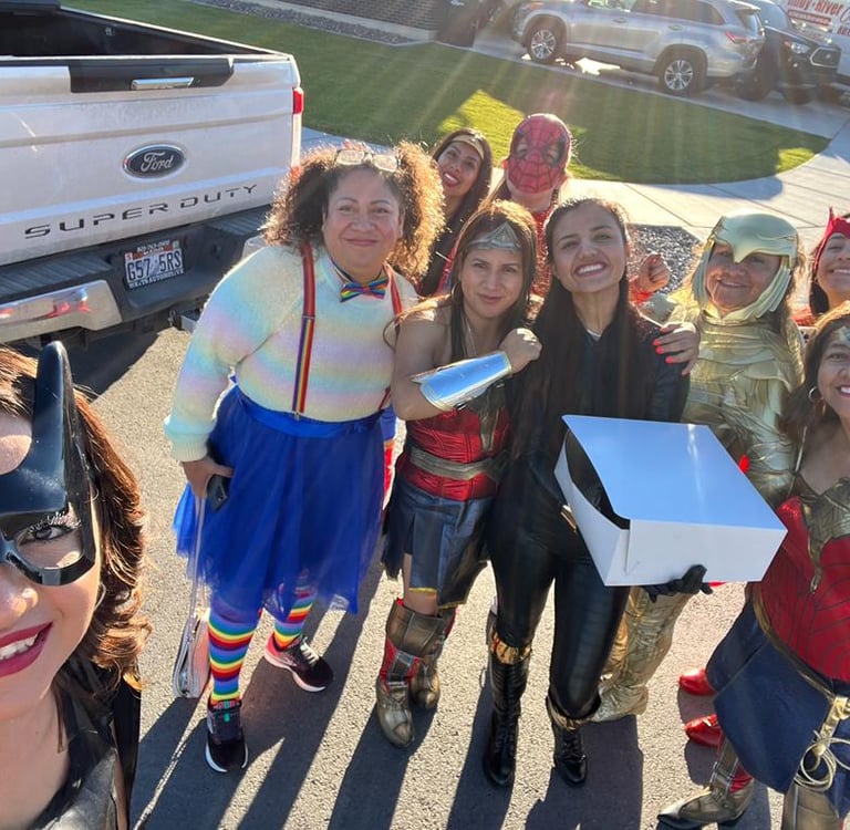 A group of people wearing colorful superhero costumes pose outdoors for a fun Halloween event.
