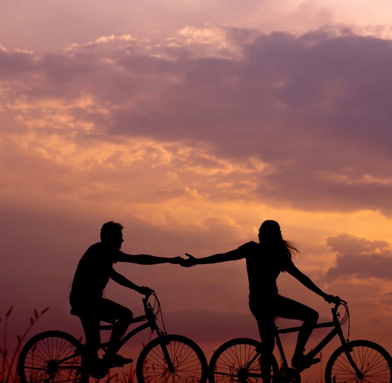 A woman reaching for her man while riding a bicycle and trying to reconnect with her man while biking through the countryside