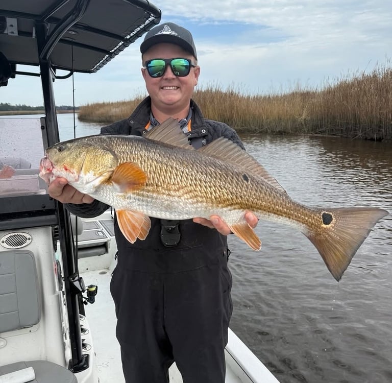 Will Bonniville holding a red drum in a coastal marsh while fishing from a boat