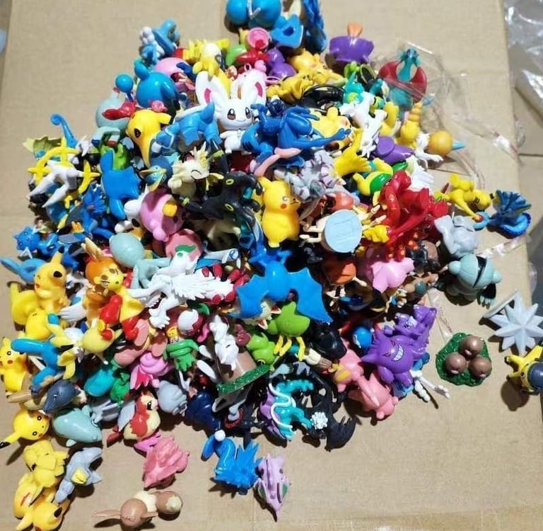 A large pile of colorful plastic Pokemon mini figures and collectible toy monsters on a cardboard surface.