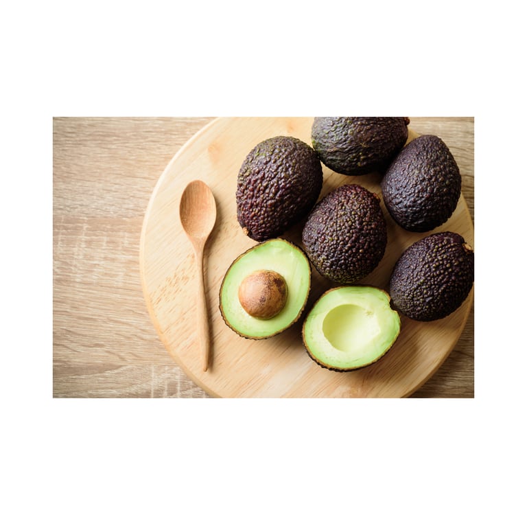 Fresh ripe Hass avocados and a wooden spoon on a circular cutting board for healthy meal prep.