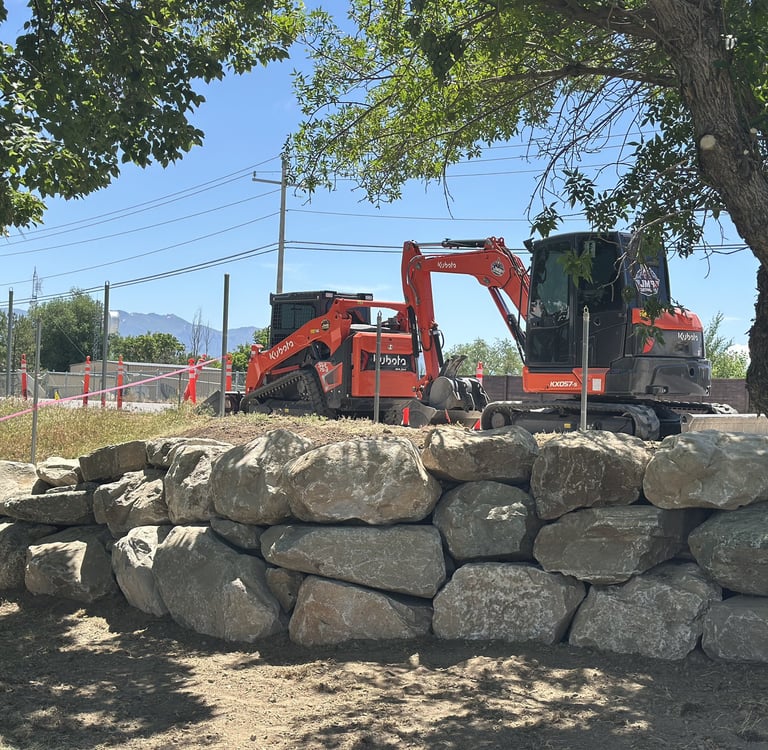 Boulder wall with Kubota skid steer and excavator sitting idle