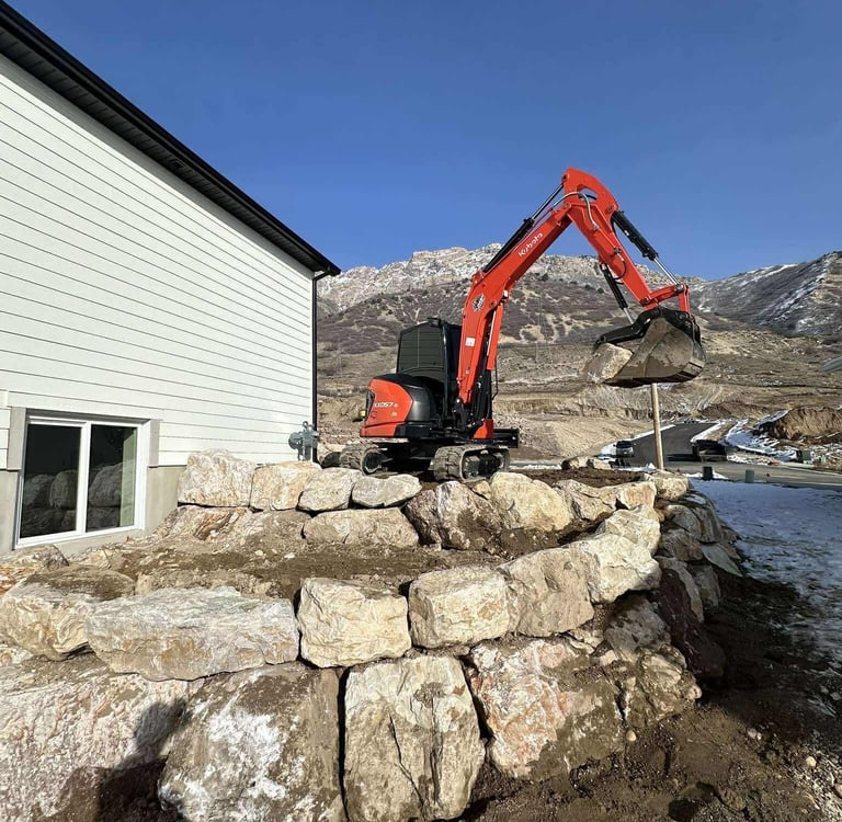 Kubota mini excavator hauling a rock as a boulder wall is being built