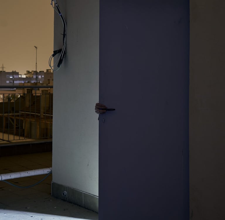 A person opening a door on a dark rooftop balcony with an outdoor light and city skyline.