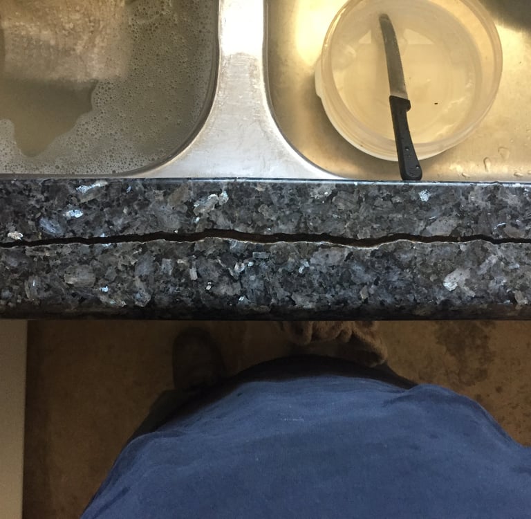 A long horizontal crack in a dark grey granite kitchen countertop next to a stainless steel sink.