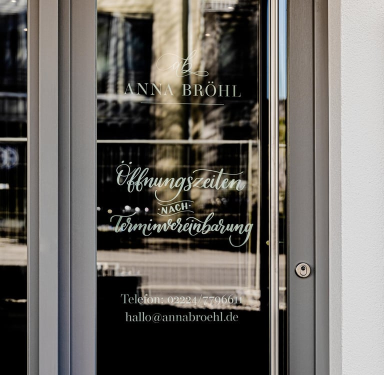 Glass entrance door to Anna Bröhl studio showing opening hours by appointment and contact details.