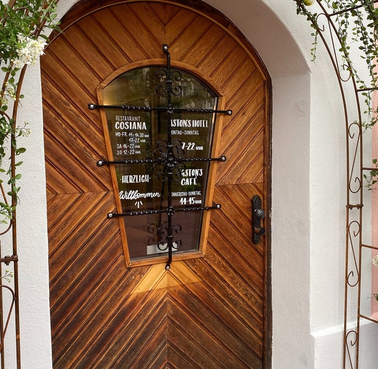 Rustic wooden door of the Cosiana Restaurant and Istons Hotel, framed by a flowering rose arch.