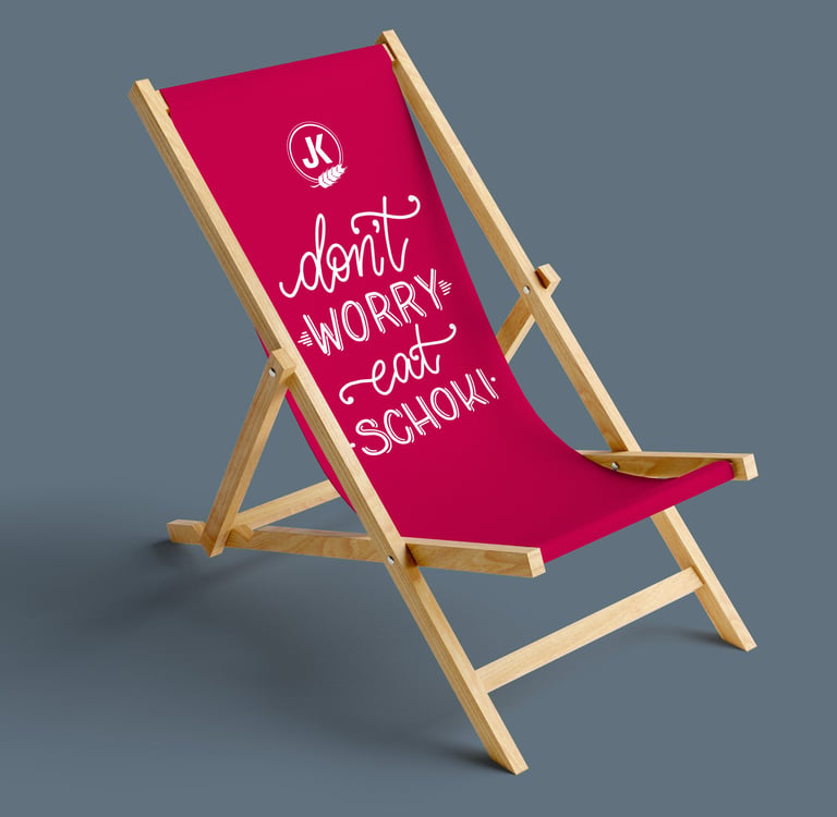 Pink folding wooden deck chair with a quote saying Don't Worry Eat Schoki for beach relaxation.