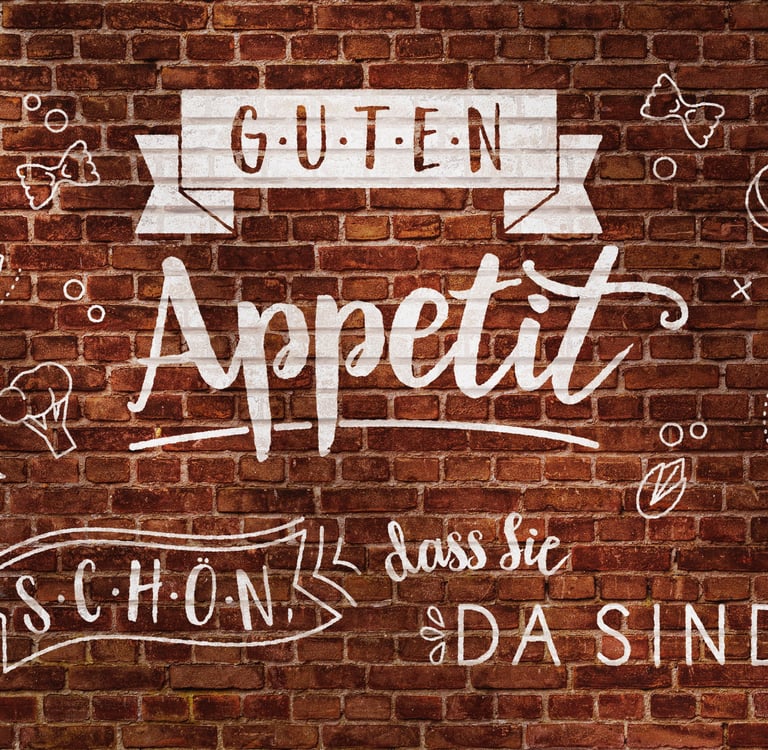 White Guten Appetit lettering and food doodles on a rustic red brick wall.