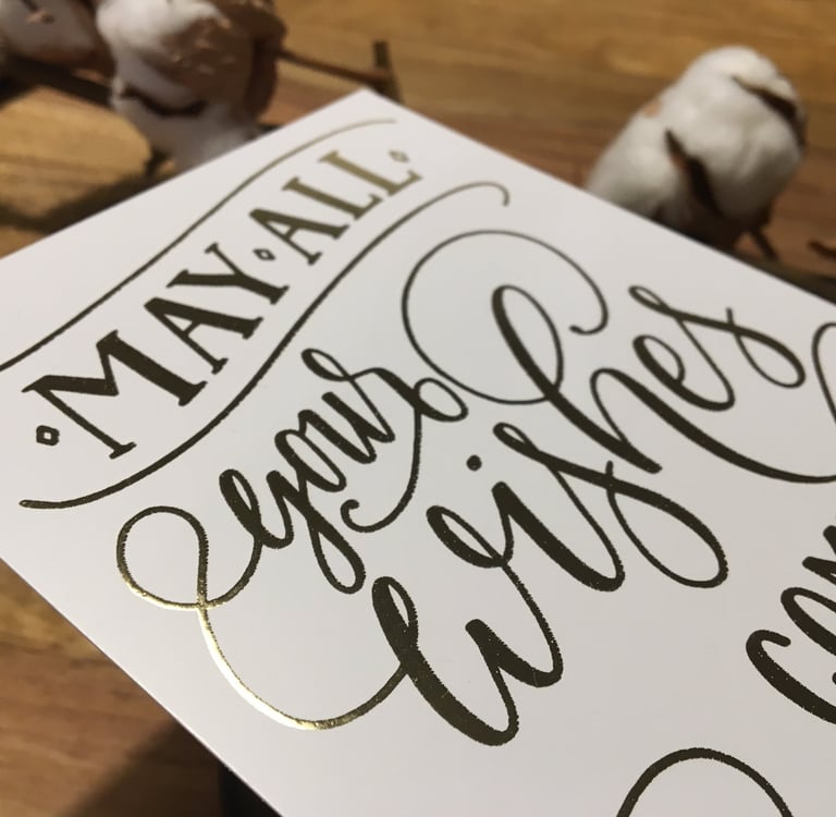 Elegant gold foil greeting card with handwritten calligraphy saying May All Your Wishes Come True.