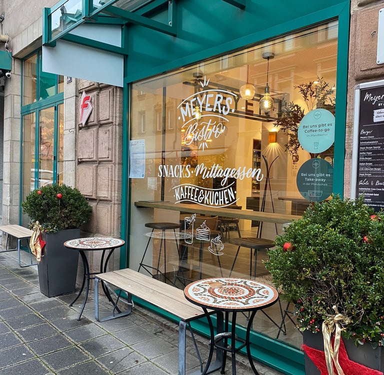 Meyers Bistro storefront with teal window frames, outdoor mosaic tables, and holiday decorations.