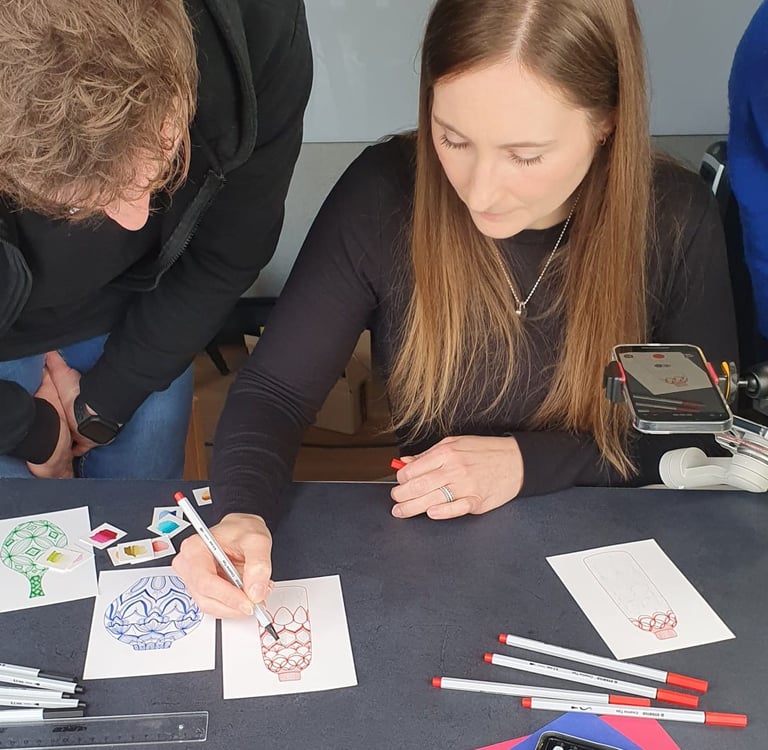 A woman uses a fine-liner pen to illustrate a creative design on paper during an art workshop.