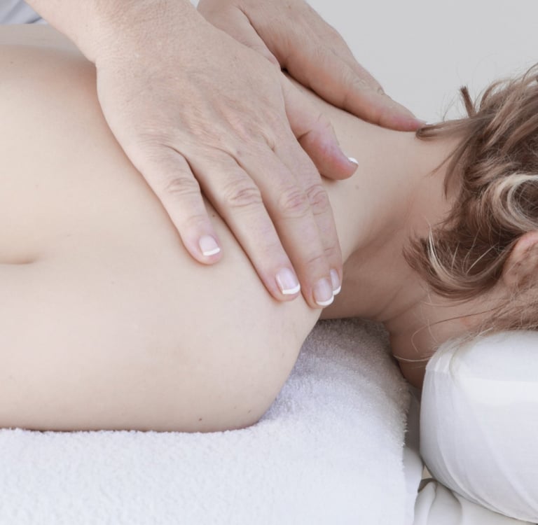 Professional massage therapist performing a therapeutic neck and shoulder massage on a relaxed female client.