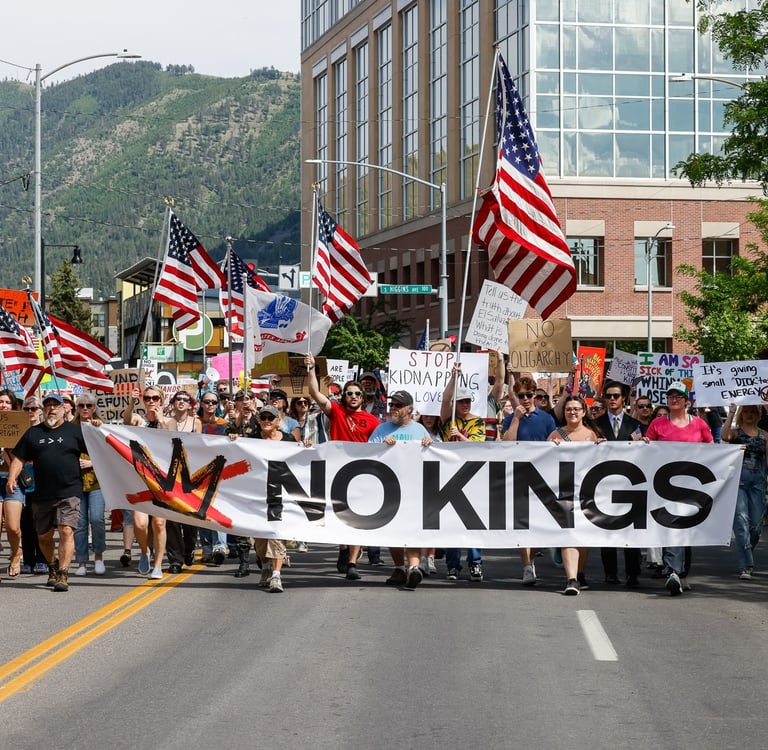 Protesters march down a city street holding American flags and a large No Kings banner during a political demonstration.