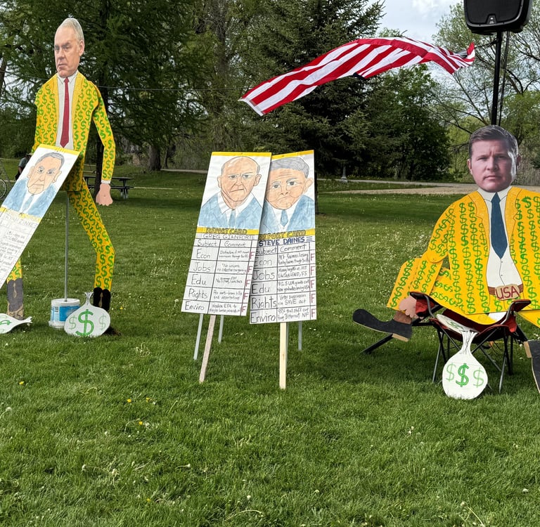 Political protest display featuring cardboard cutouts of candidates in dollar sign suits for a rally.