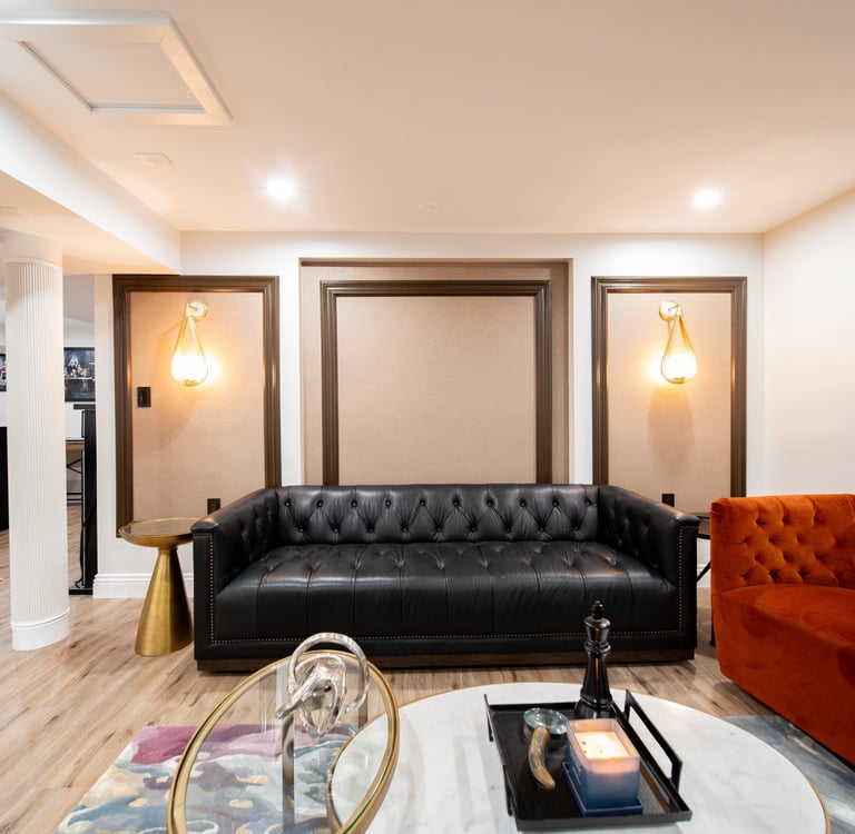 Modern luxury lounge featuring a black tufted leather sofa and orange velvet armchair with elegant wall sconces.