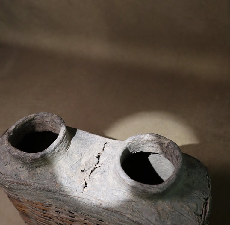 Antique woven wicker basket bottle with two clay ceramic openings under spotlight.