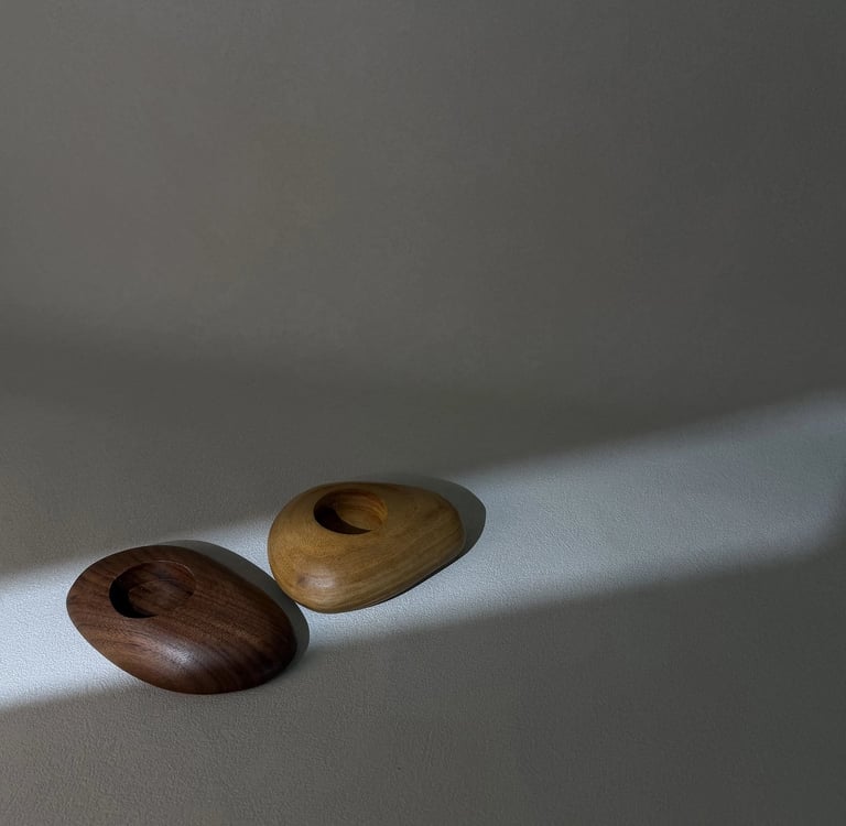 Two smooth pebble-shaped wooden tea light holders in dark walnut and light oak finishes.