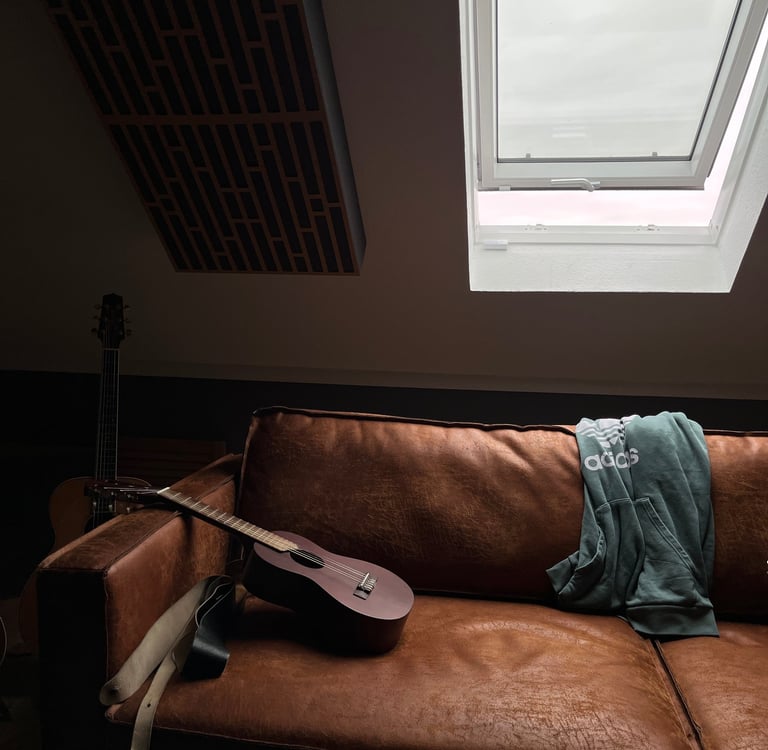 Guitar resting on leather couch under roof window in studio room