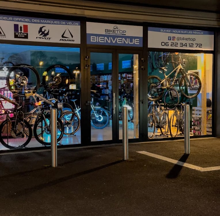 Biketop store front displaying mountain bikes and road bicycles through glass windows at night.