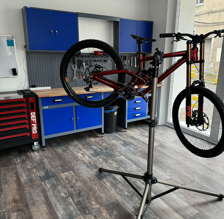 Red mountain bike on a professional repair stand in a modern bicycle workshop with blue tool cabinets.