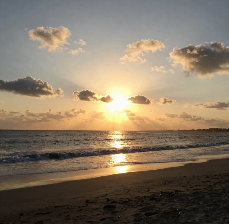 Golden sun setting over a calm ocean beach with gentle waves and scattered clouds.