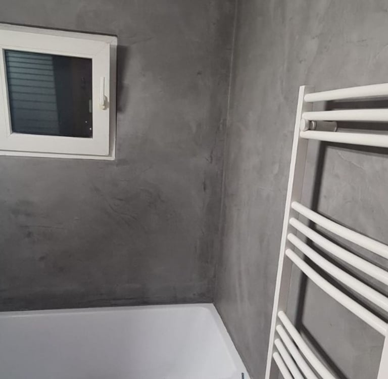 Modern bathroom with grey microcement walls, a white bathtub, and a heated towel rail.