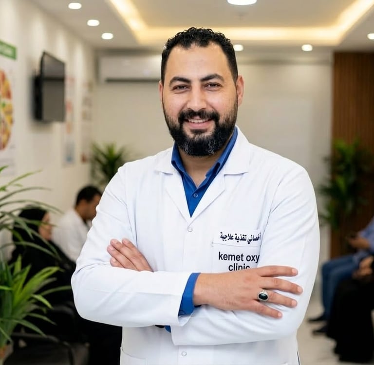 Smiling Mohamed Hassan, Therapeutic  in a white coat at Kemet Oxy Clinic standing with arms crossed.