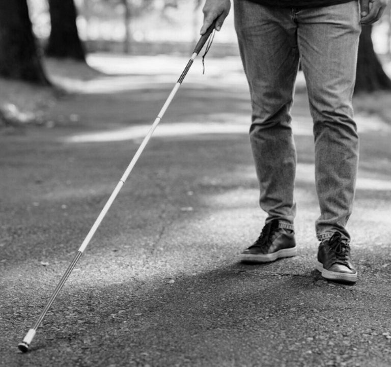 Niewidomy mężczyzna porusza się za pomocą białej laski w ścieżce.