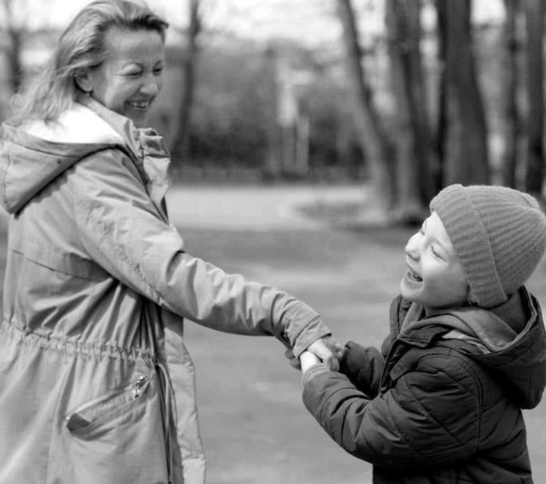 Usmiechnięty chłopiec z wadą wzroku wraz z mamą na ścieżce wśród drzew.