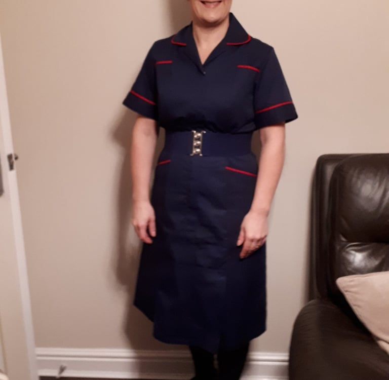 Smiling healthcare professional in a navy blue nurse uniform with red trim and a silver buckle belt.