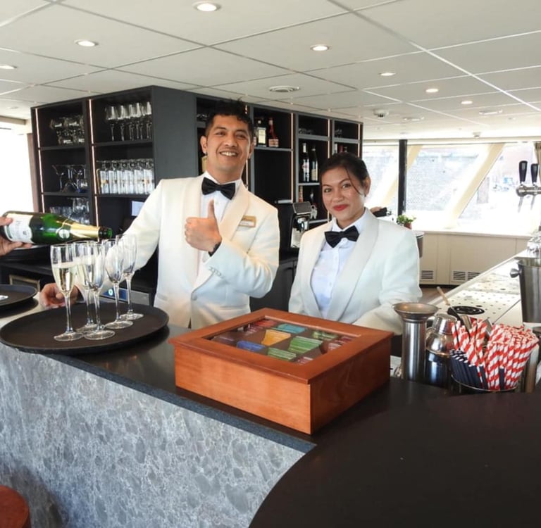 Waitstaff in white tuxedos pouring champagne at a luxury cruise ship bar.