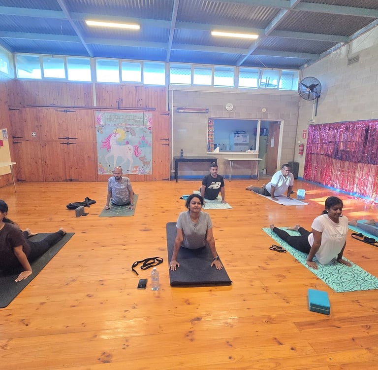 A group of people practicing cobra pose during a yoga class in a studio with wooden floors.