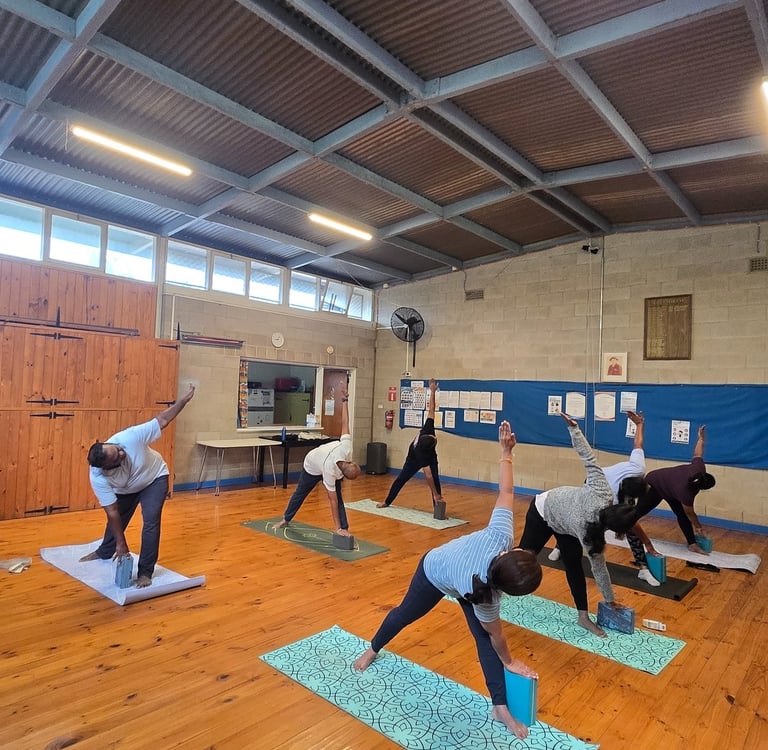 Group yoga class practicing triangle pose with foam blocks on mats in a studio.