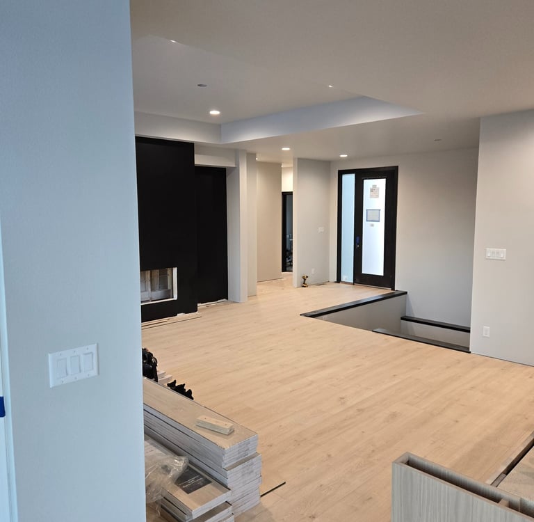 Modern home interior renovation featuring light oak luxury vinyl plank flooring and black fireplace wall.