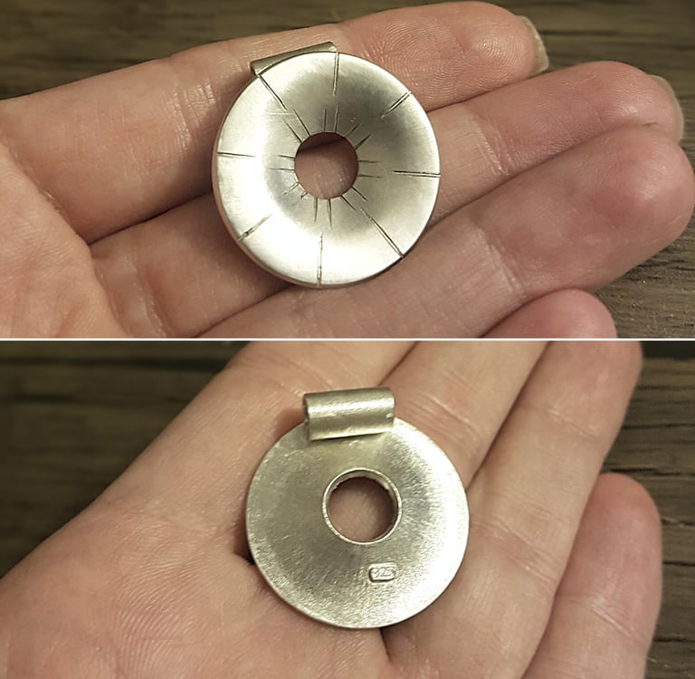 Handcrafted round sterling silver pendant with sunray etched lines held in a person's hand.