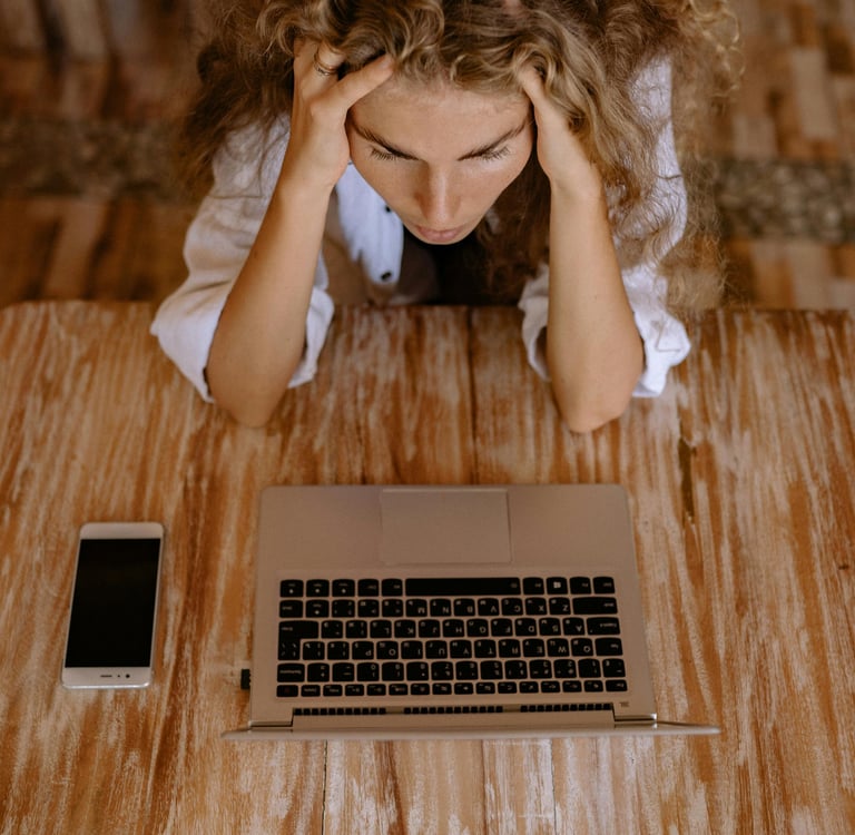 a woman sitting at a table with a laptop and a cell phone