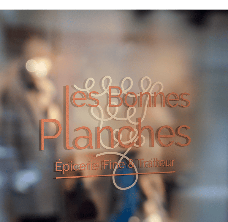 Logo Les Bonnes Planches appliqué en lettrage sur la vitrine d'une épicerie fine.