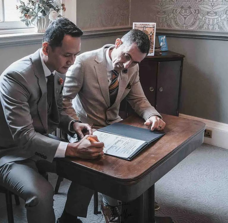A gay couple in elegant suits signing their marriage certificate during a wedding ceremony.