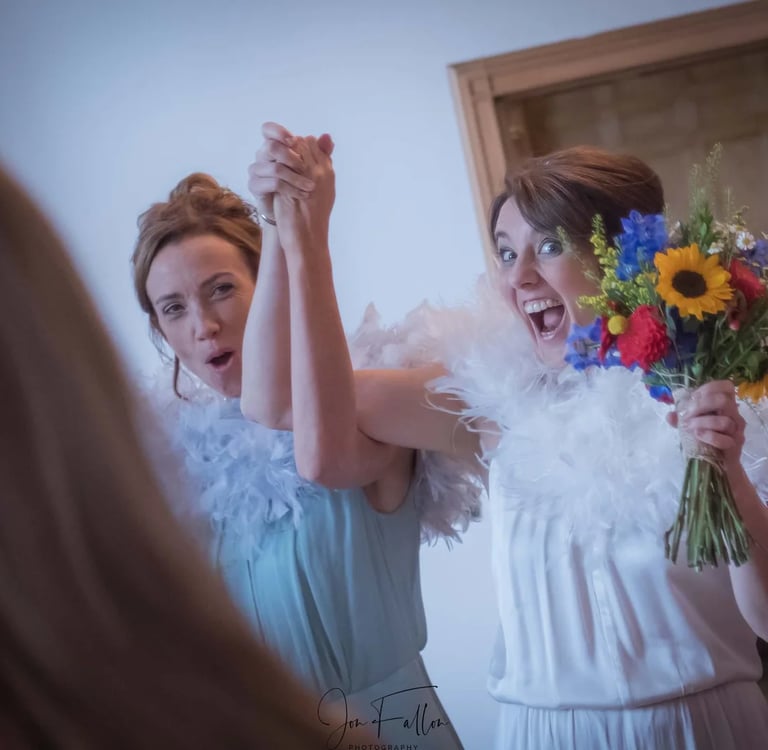 Two brides wearing white feather boas celebrate at a wedding reception.