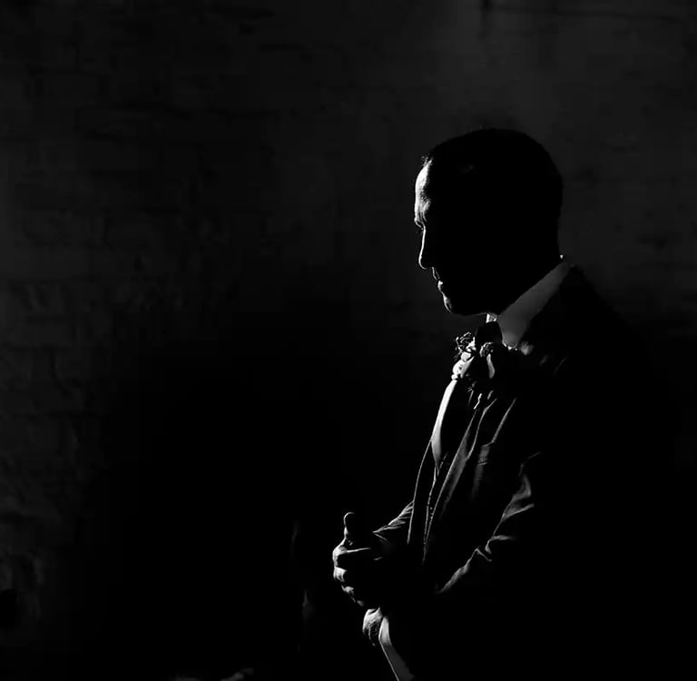 Black and white silhouette of a groom in a tuxedo standing by a window before a wedding ceremony.