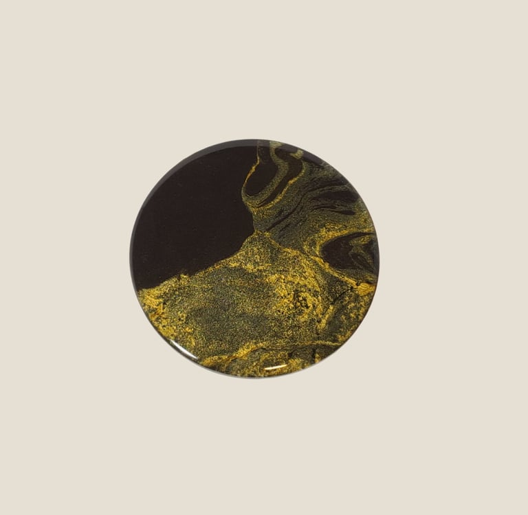 Resin coaster with abstract black and shimmering gold volcano design..