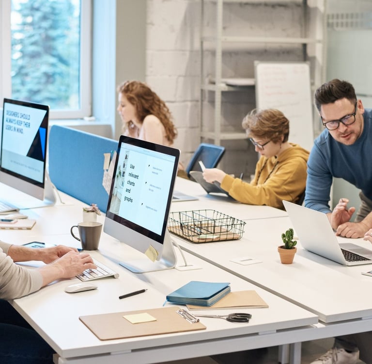 Diverse creative team collaborating on web design projects in a bright, modern open-plan office.